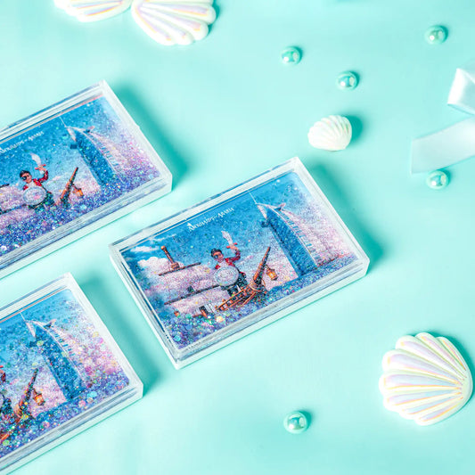 Three small rectangular boxes with mermaid illustrations on a turquoise background with shells and pearls.