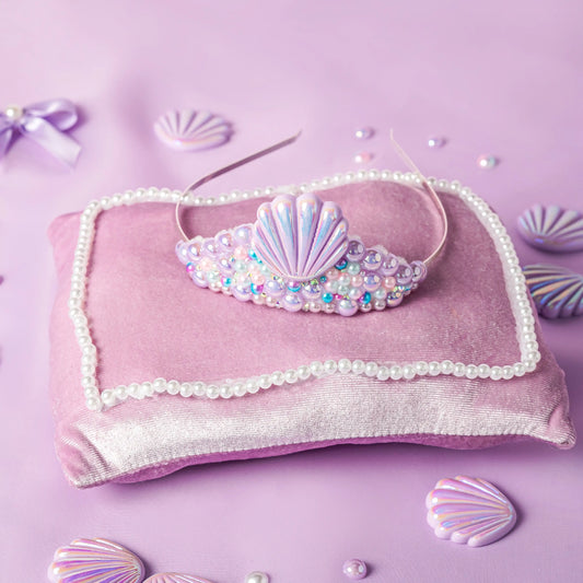 Mermaid-themed headband with seashell design on a pink pillow with shell decorations.