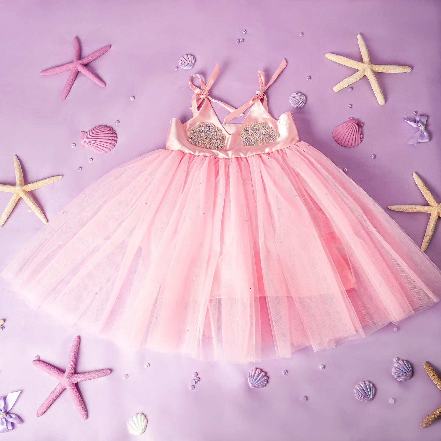 Pink tulle dress with embellishments on a purple background with starfish and shells.