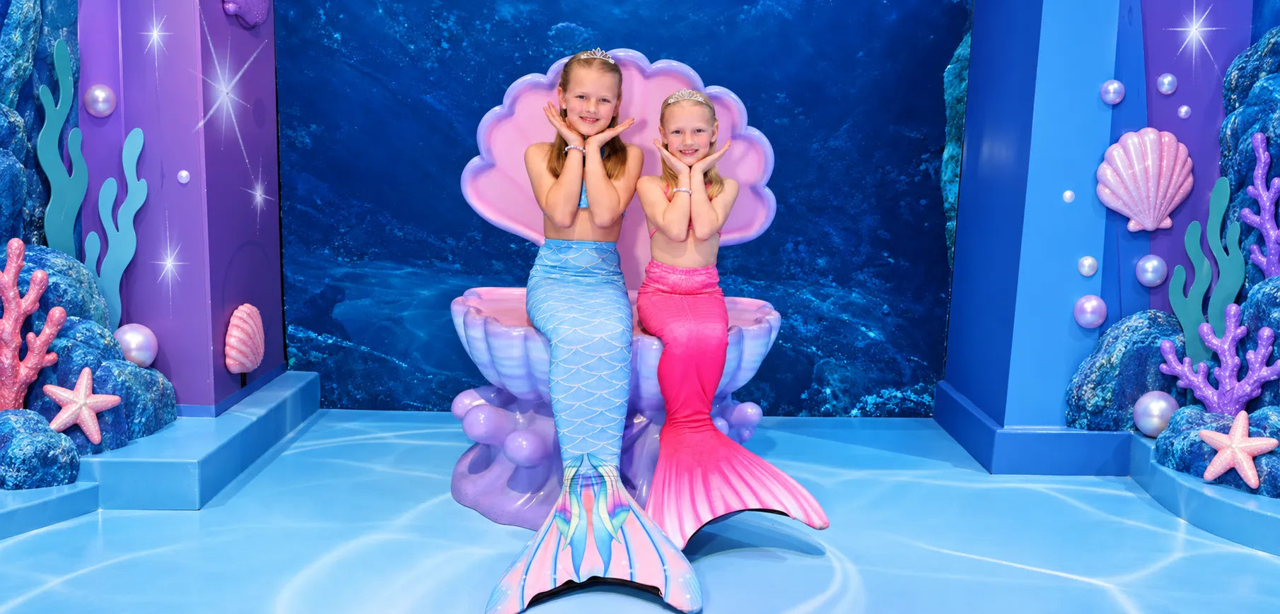 Two children in mermaid tails in the giant shell at Mermaids of Arabia