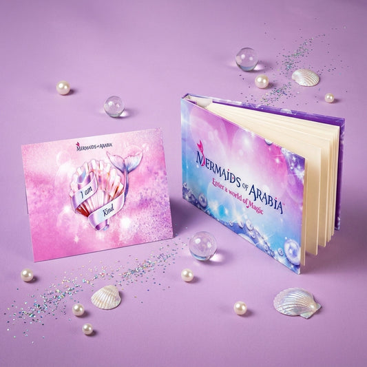 A decorative book and matching card set styled on a lavender surface with pearls, shells, and glitter. The book cover reads 'Mermaids of Arabia' and shows a pastel mermaid tail and ocean-themed artwork.