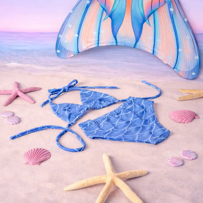 Blue mermaid-patterned bikini set on a sandy beach with starfish and shells.