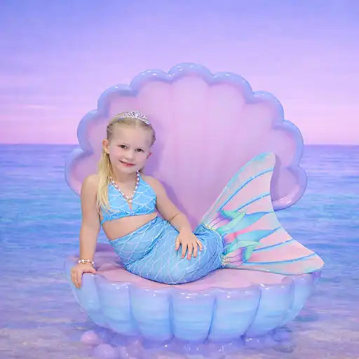 Child in a mermaid costume sitting on an inflatable shell with a pastel ocean background