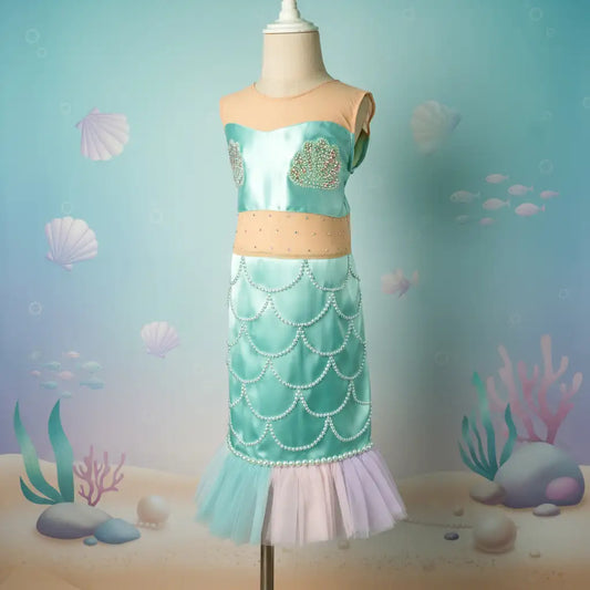 Mermaid-themed dress on a mannequin against an underwater background with shells and corals.
