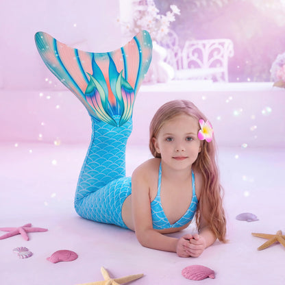 Young girl in a mermaid tail with a colorful tail and pink hair accessory, surrounded by starfish and shells on a soft pink background.