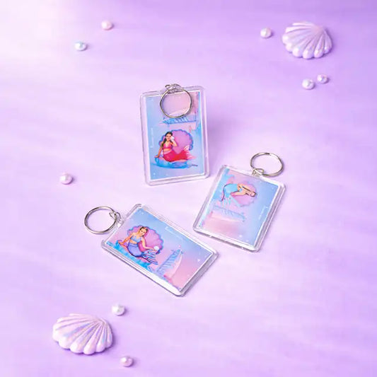 Mermaid-themed keychains on a purple background with shells and pearls.
