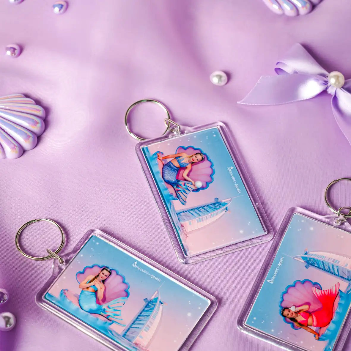 Mermaid-themed keychains on a purple background with decorative elements.