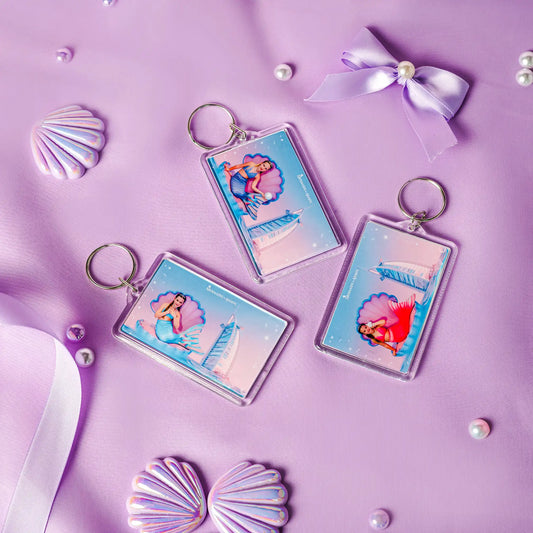 Three mermaid-themed keychains on a purple background with shells and ribbons.