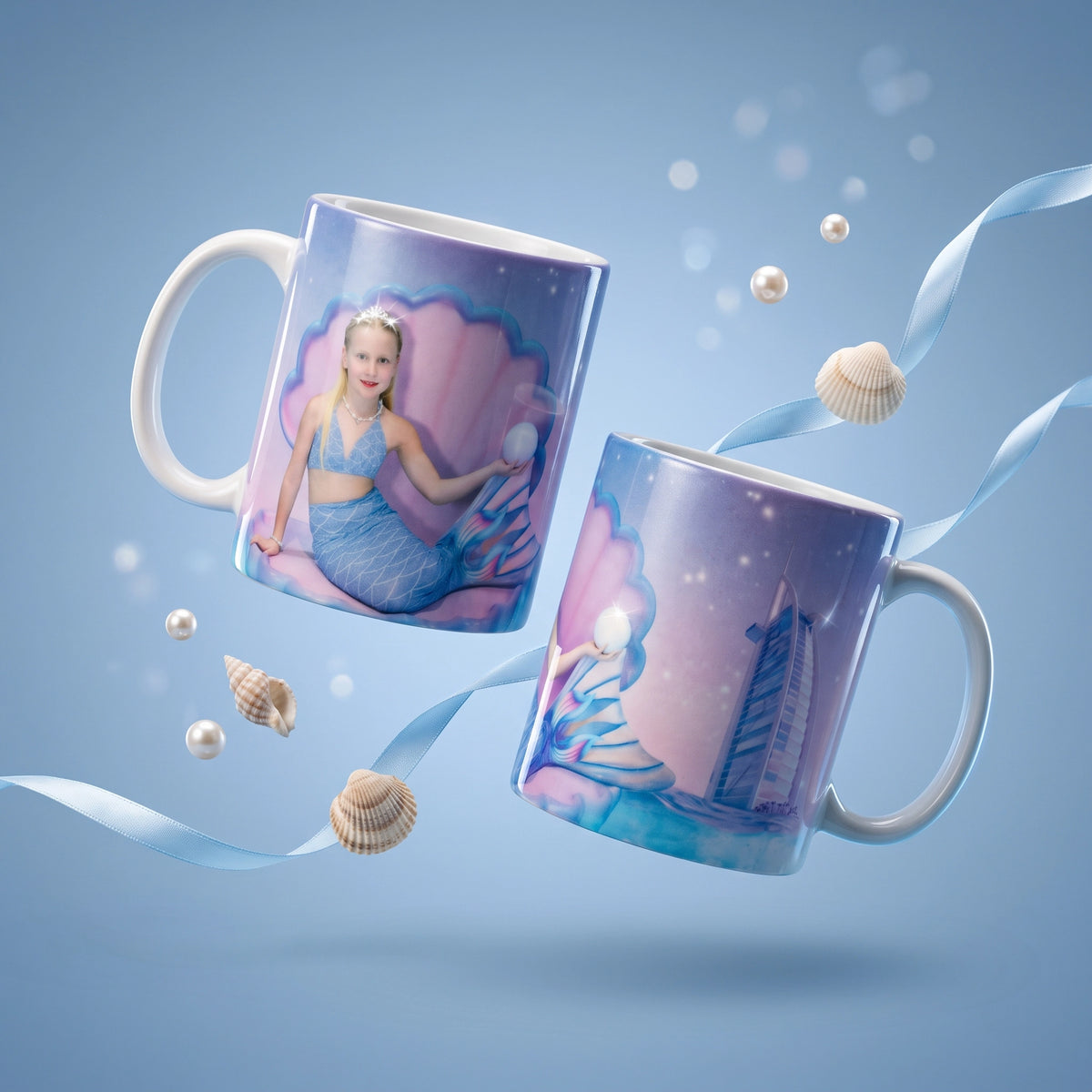 Two white ceramic mugs with custom printed designs floating against a light blue background with decorative ribbons, shells, and pearl-like spheres. One mug shows a mermaid illustration, and the other shows a sailboat scene.
