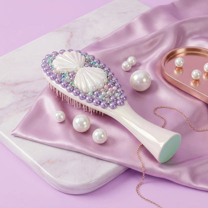 A decorative hairbrush with a white handle and shell-shaped bristles, embellished with purple pearls and pastel beads, styled on a pink satin cloth with faux pearls and a rose-gold tray on a lavender background.