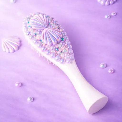 Decorative hairbrush with seashell and pearl details on a purple background