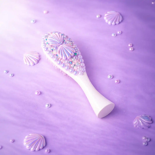Decorative hairbrush with shell and pearl design on a purple background