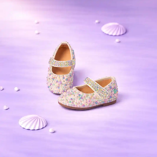 Pair of sparkling children's shoes on a purple background with seashells.