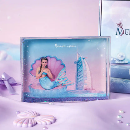 Mermaid-themed product packaging with a building and seashell design on a light purple background.