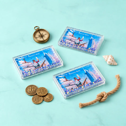 Three clear rectangular boxes containing blue and purple glitter with a printed New York City skyline scene and the words 'New York City' are arranged on a light aqua background with decorative nautical props including a compass, coins, a shell, and a rope.