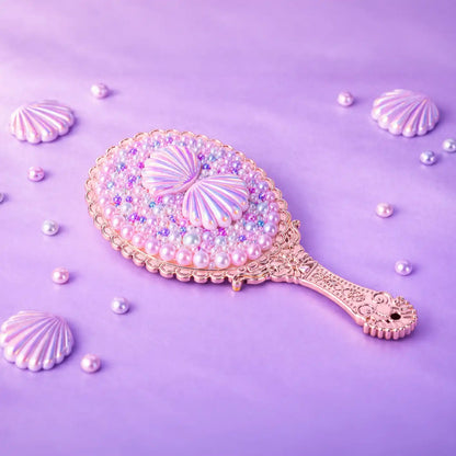 Decorative hand mirror with shell and pearl design on a purple background