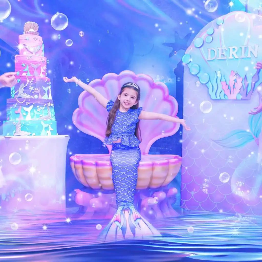 Mermaid-themed birthday party setup with a child in a mermaid costume and cake.