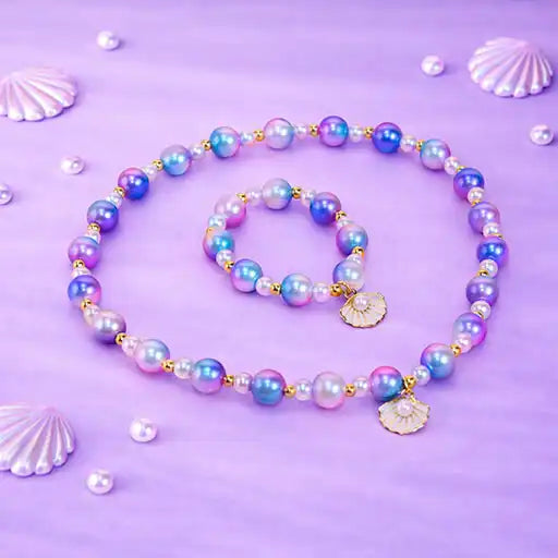 Pearl necklace and bracelet set on a purple background with seashells.