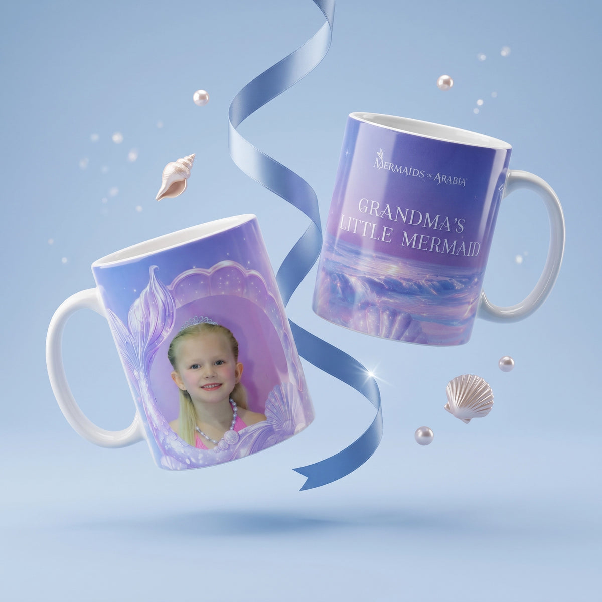 Two custom ceramic mugs with mermaid-themed purple and blue designs, floating against a light blue background with decorative seashells and a blue ribbon. One mug shows a printed portrait of a young girl, and the other has the text 'GRANDMA'S LITTLE MERMAID' and 'MERMAIDS - ARVIA'.