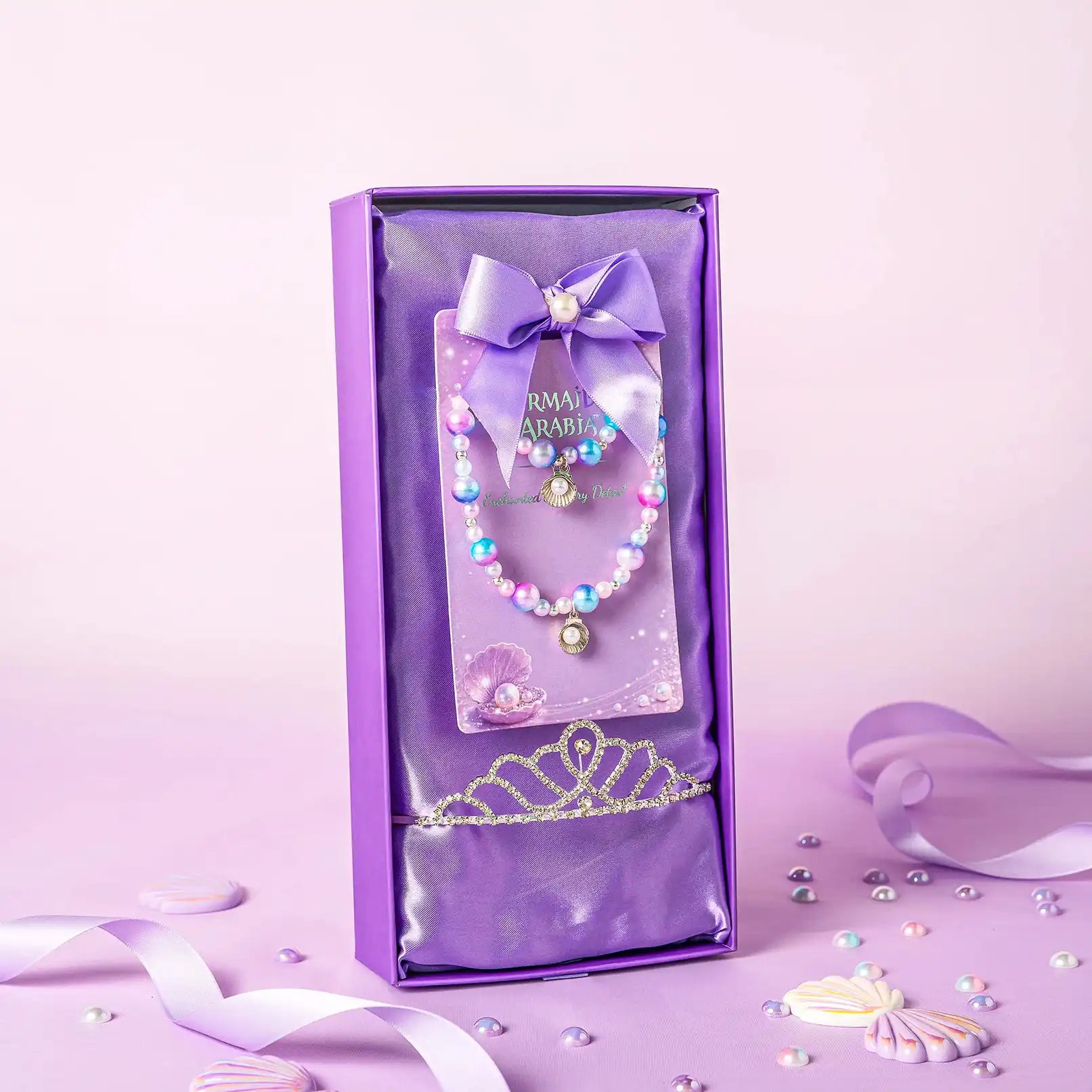 Purple jewelry set with bracelet, bow, and tiara in a box on a pink background