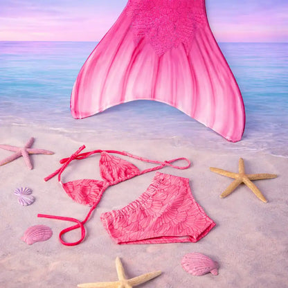 Pink mermaid tail and bikini set on a sandy beach with starfish and shells.