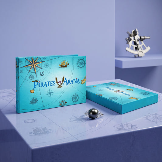 A turquoise pirate-themed jewelry box set with nautical illustrations, shown alongside a ring with a dark pearl on a light blue surface. The packaging features the text 'PIRATES OF ARABIA' and decorative compass, ship, and anchor motifs.