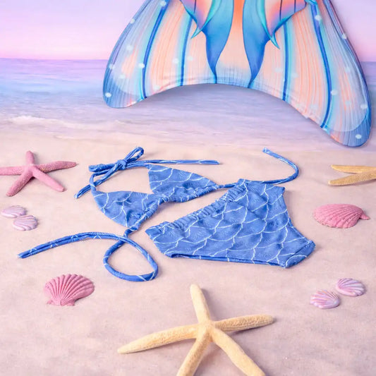 Blue mermaid-patterned bikini set on a sandy beach with starfish and shells.