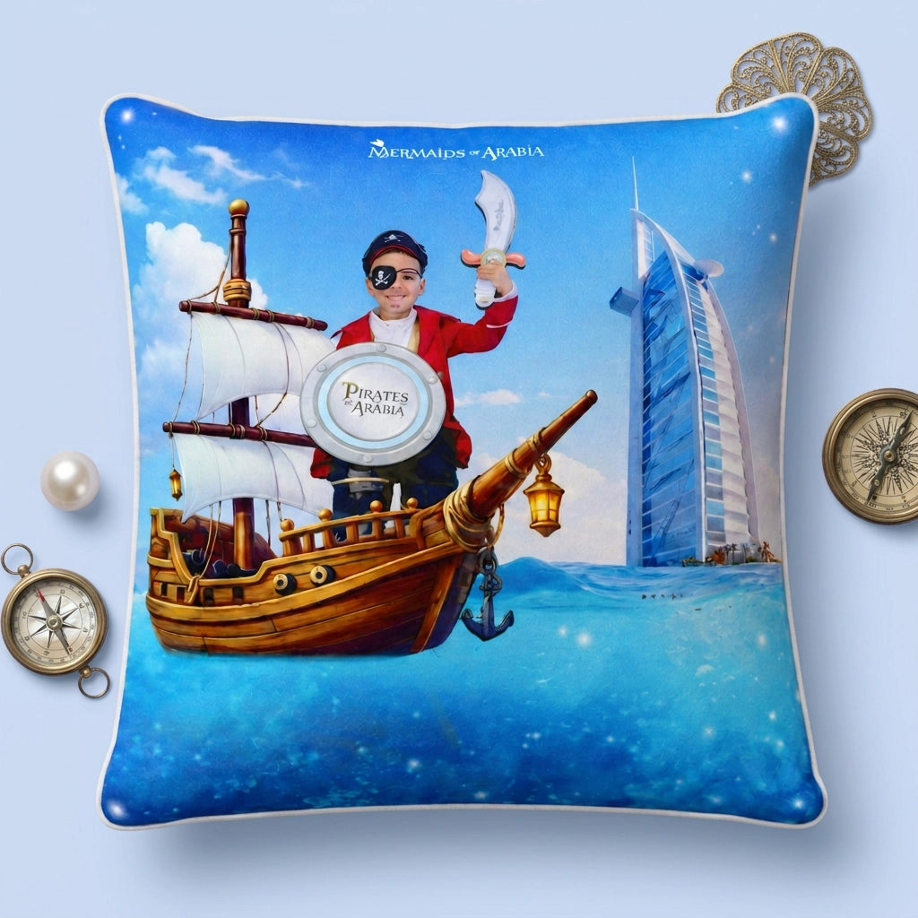 A square decorative throw pillow featuring a colorful pirate-themed illustration with a ship, a person in pirate attire, and the Burj Khalifa on a blue ocean background. The pillow is displayed on a light blue surface with decorative props including a pearl, compass, and coin.
