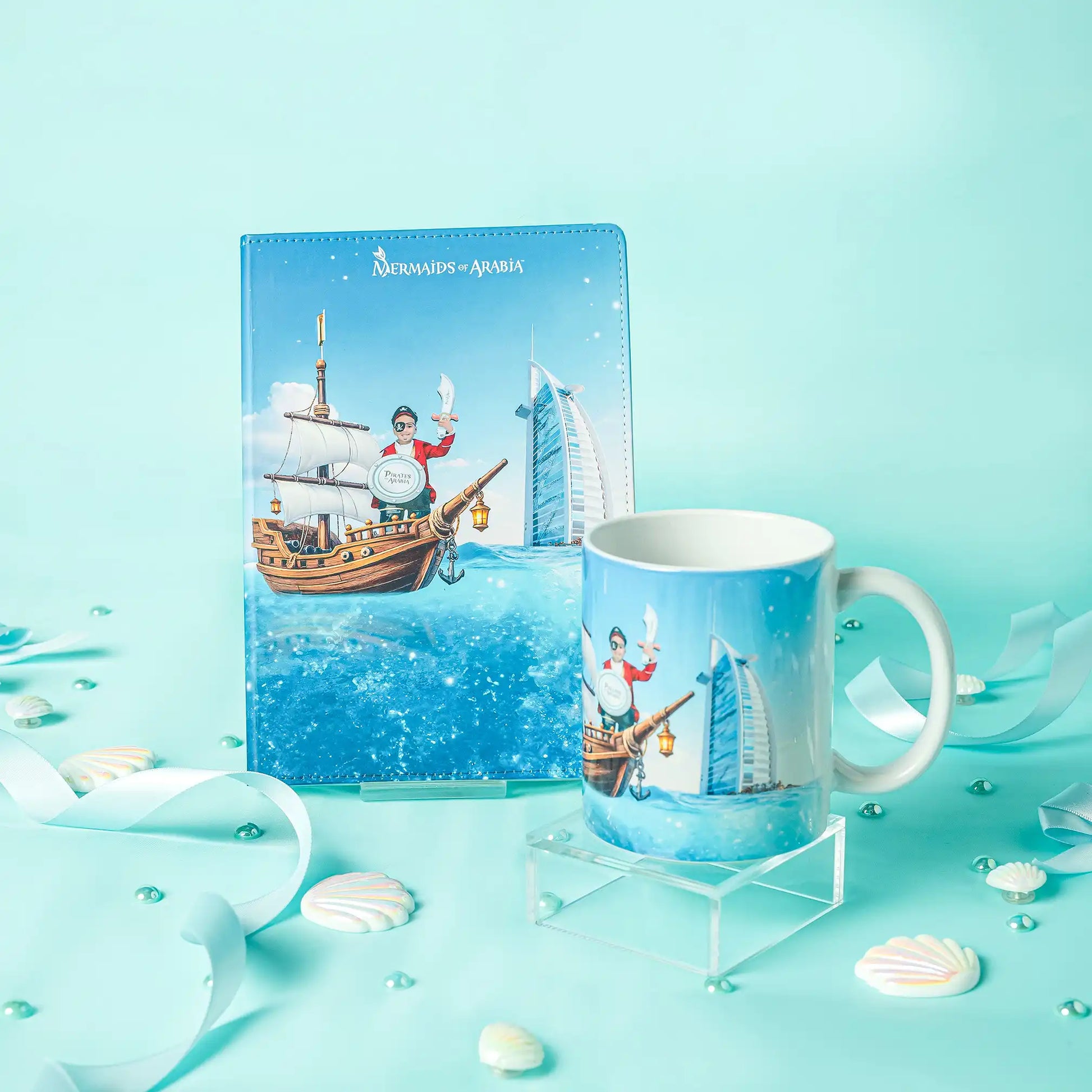 Notebook and mug with a ship and mermaid design on a light blue background