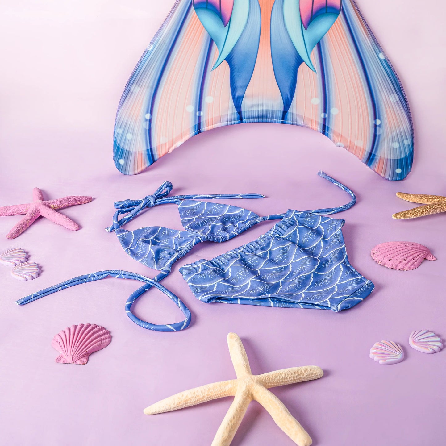Blue bikini set with mermaid tail and sea-themed accessories on a pink background