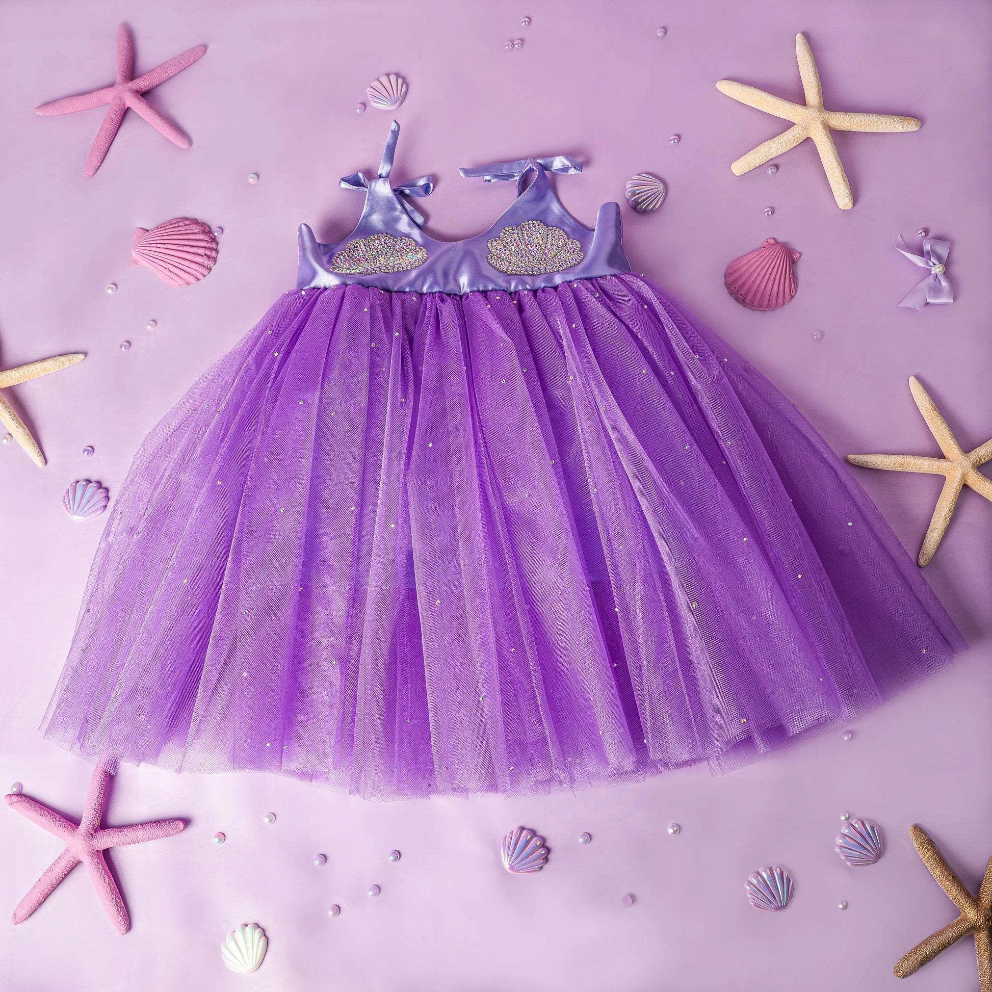Purple dress with starfish and shell decorations on a pink background