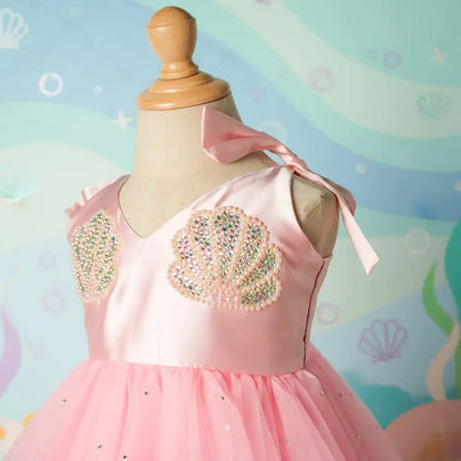 Pink dress with shell designs on a mannequin against a colorful mermaid-themed background