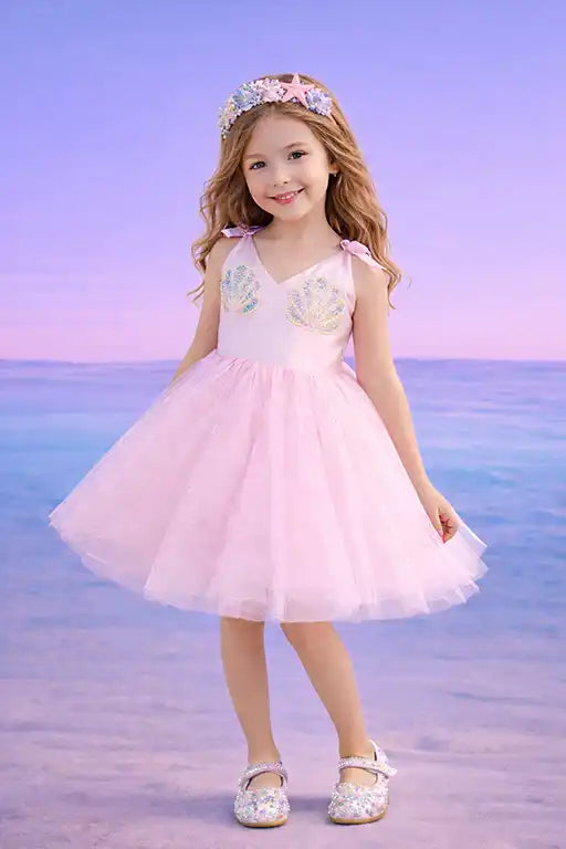 Young girl in a pink dress with floral details standing on a beach with a purple sky.