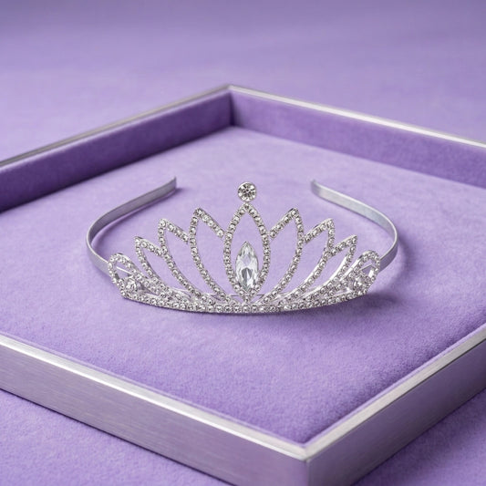 A silver tiara with clear rhinestones and a central marquise-cut crystal, displayed on a purple velvet-lined jewelry box.