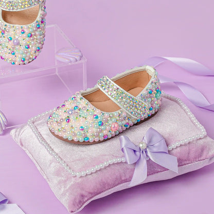Decorative children's shoe with pearls and crystals on a pink cushion with a bow.